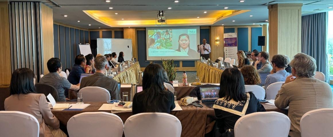 Vue d’ensemble d’une salle de conférence où des chercheurs et partenaires sont assis autour de tables, écoutant un intervenant présenter des diapositives sur l’agroécologie et les systèmes alimentaires lors de la réunion annuelle de MALICA.