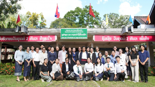Un grand groupe de personnes, comprenant des chercheurs, des étudiants et des formateurs, posent ensemble devant la Faculté d'agriculture du Laos, sous une pancarte et des drapeaux nationaux.