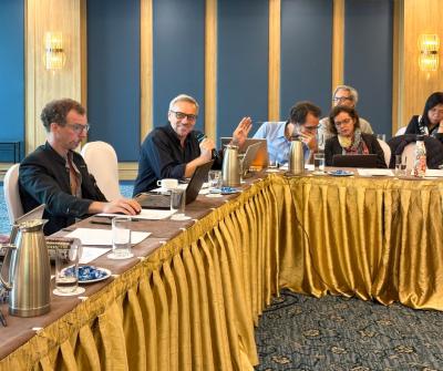 Un participant s&rsquo;exprime au micro pendant une session, tandis que d&rsquo;autres participants &eacute;coutent et prennent des notes autour de la table.