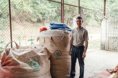 Mr. Lo Van Muu, a farmer from Na Sang 1 village in Dien Bien province, stands beside large silage bags marked with the ASSET project logo.